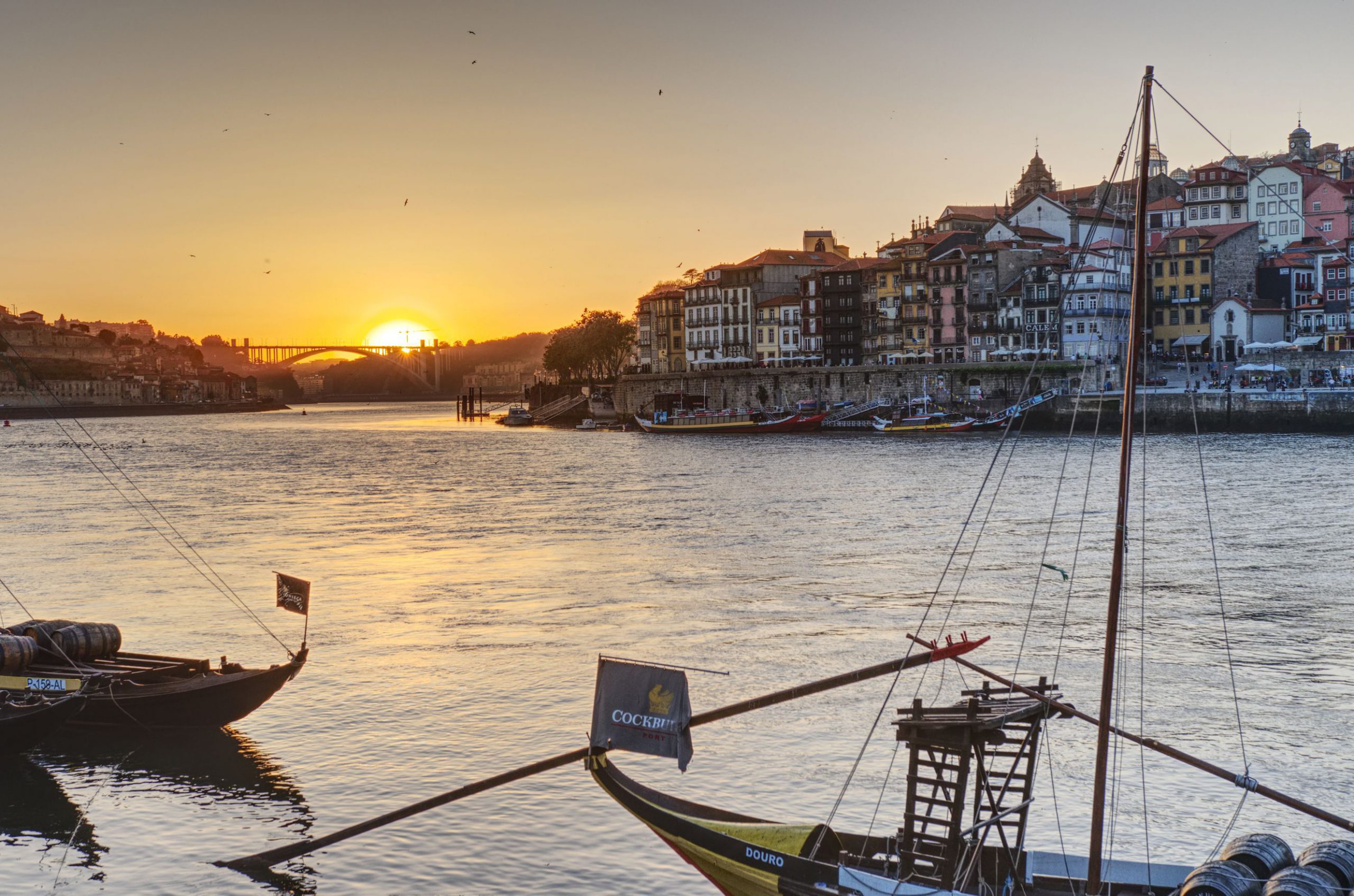 The sun goes down over the sea, in the foreground one of the Douro bridges of Porto