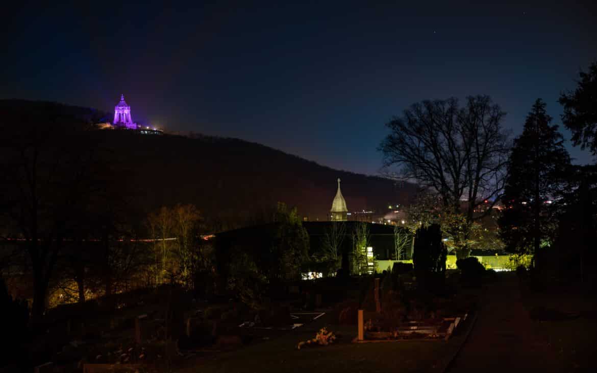 Kaiser Wilhelm Monument illuminated in pink on the occasion of World Breast Cancer Day. Hausberge cemetery and Porta Westfalica town hall in the foreground.